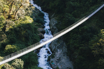 Suspension bridge hanging from a cliff with a river below in the background.