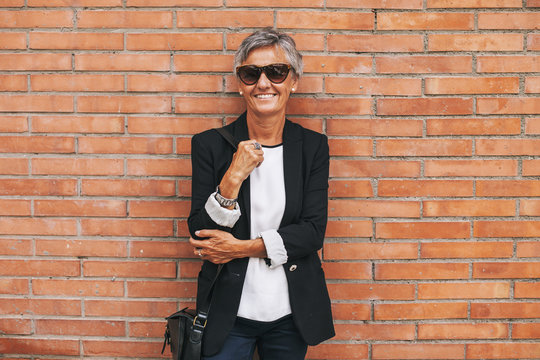 Mature businesswoman looking camera in front brick wall.