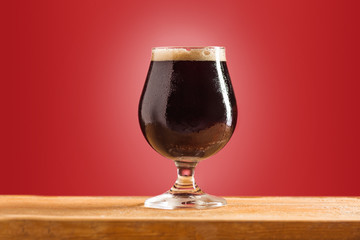glass of cold frothy dark beer on an old wooden table