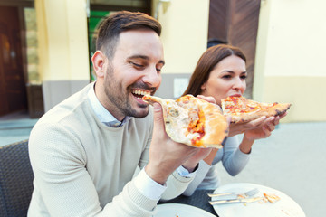 Couple eating pizza snack outdoors.