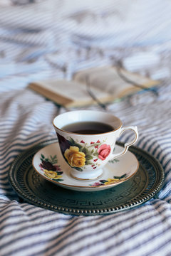 Black tea in china cup on vintage tray with open book and glasses