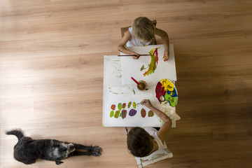 Children painting on table with dog lying on floor