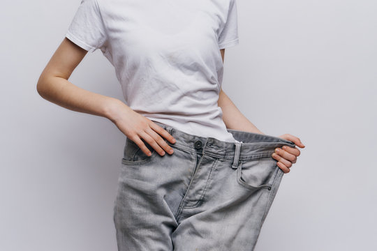 A Woman In A White T-shirt And Pants That Are Too Big For Her