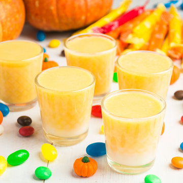 Pumpkin smoothie on white table with candies