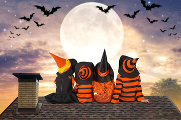 Halloween.Children in costumes of witches and wizard are sitting that night on the roof and look at...