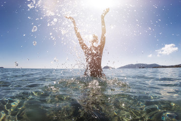 Junge Frau steht im Meer und spritzt mit Wasser