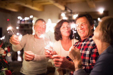 Senior friends with sparklers next to Christmas tree having fun.