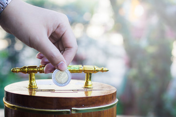 Hand holding coin drops into a wooden piggy bank with light and copy space. Saving coin concept. Conceptual saving money for future. Concept saving money background. Investment money Concept.