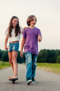 Boy looking macho while pulling smiling girl on a skateboard forward