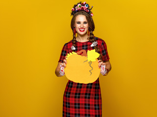 smiling modern woman in halloween costume showing pumpkin