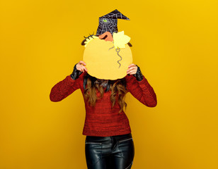 woman on yellow background holding pumpkin in front of face