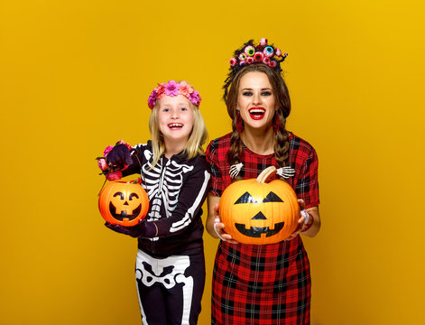 smiling mother and daughter showing jack-o-lantern pumpkins