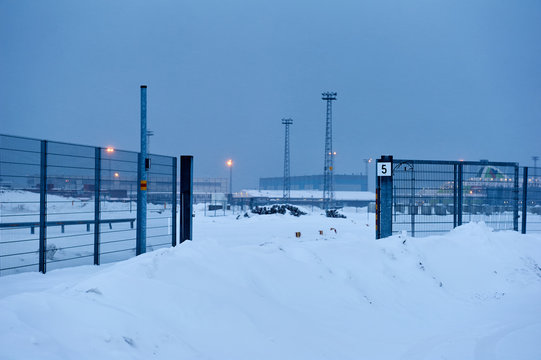 Light posts and fence and gate in snow on a lightless winter evening in Helsink, Finland