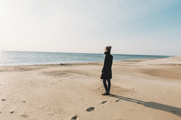 Woman walking on sandy shore near the sea.