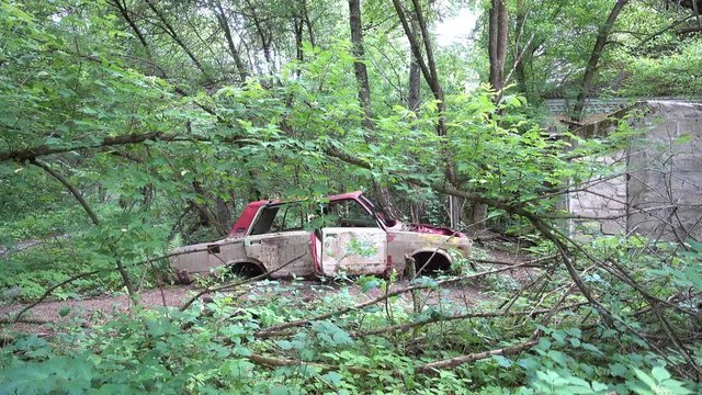 Chernobyl, Ukraine - 17th of June 2017: Visit to Zalesye village in Chernobyl zone - 4K Carcass of an old car near abandoned house