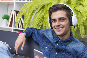 young man listening to music in the home Lounge with phone and earphones