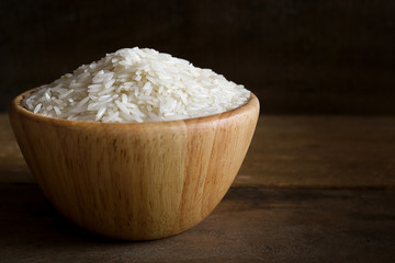 Jasmine rice in wooden bowl on rustic wood background