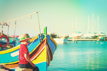 Obraz premium little boy looking at traditional boats in Malta