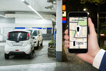 Hand with phone on a background of electric cars charging point. E-car sharing concept