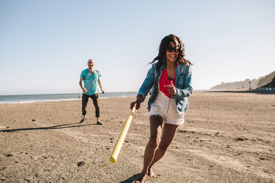 Happy beautiful woman playing baseball on the beach