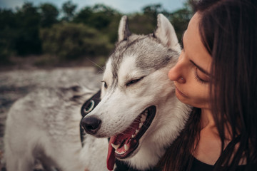 Beautiful girl plays with a dog (grey and white husky) in the mountains at sunset