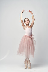 little ballerina in a light bundle and pointe poses with her arms raised
