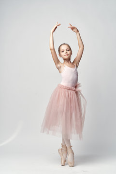 Fototapeta little ballerina in a light bundle and pointe poses with her arms raised