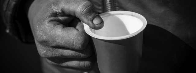 Dirty Beggar Hand Holding Plastic Cup. Poor Man Begging for Money on the Street Close Up.