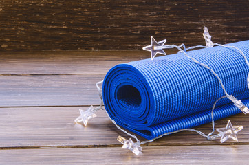 Blue exercise mat with Christmas garland on wooden background. Training on Christmas Day concept. Sport xmas concept. Copy space. © vasanty
