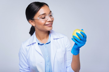 Pleasant lab worker looking at apple in her hands