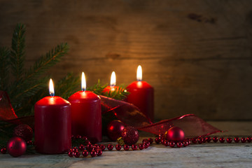 Four red burning candles at the fourth advent, christmas decoration with spruce twigs and baubles on a rustic board, wooden background with copy space