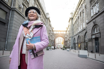 Fototapeta na wymiar Excited senior lady standing with journal on street