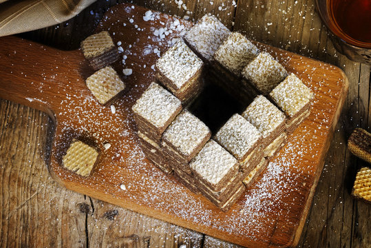 Waffle cookies built to an impossible penrose stairs, which always goes upwards, diet metaphor for eating more and more sweets, rustic wooden background