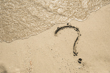 Question mark sign on sand beach near the sea and waves