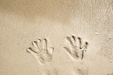 A trace of hands on the wet sand near the sea and waves