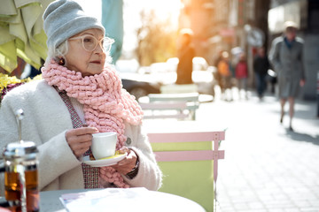 Pensive mature lady sitting outside with mug of coffee