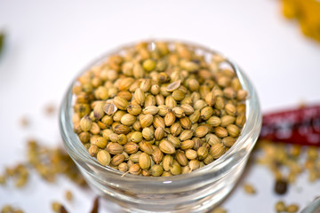 A close-up view of a glass bowl filled with whole coriander seeds, highlighting their rich texture and warm golden-brown color. The seeds are commonly used in Indian, Asian, and Middle Eastern cuisine