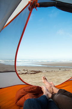 Couples sandy feet sticking out of tent camping on the beach