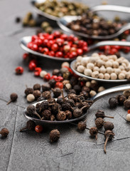 Colorful peppers in spoon on black table - cubeb, pink, green and white closeup. Spices. Selective focus
