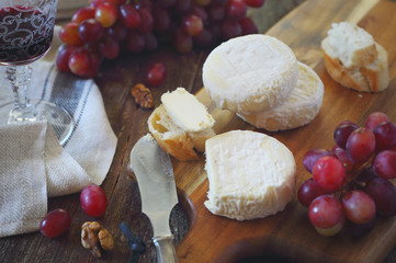 French Goat cheese, red grapes and glass of red wine on wooden cutting board. Toned image, focus selective