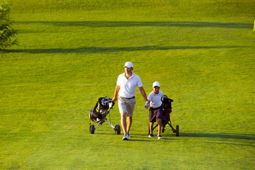 man with his son golfers walking on perfect golf course at summer evening