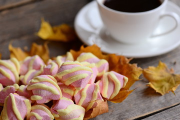 Light pink and yellow marshmallow on yellow autumn leaves, coffee cup on a vintage wooden background. Nice autumn coffee break concept. Closeup