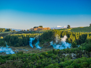 Geothermal steam fissures in a valley with snow capped mountains in the background