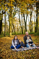 Naklejka na ściany i meble Happy caucasian family of mom dad and little girl with boy sitting on plaid at majestic autumn fall forest.