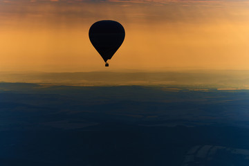 Aerial view of summer countryside during sunset with silhouette of hot air balloon