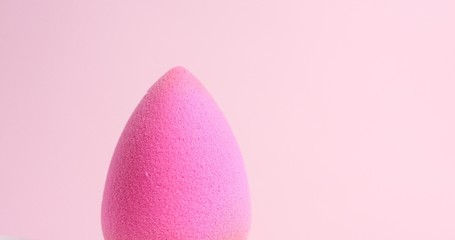 Slowly pouring liquid beige makeup foundation or bb cream on a clean pink sponge on light pink background