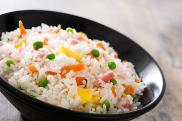 Chinese fried rice with vegetables and omelette in black bowl  on wooden table
