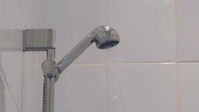 A jet of water from the shower hear. Close-up. White shower and water pressure switch on and off.