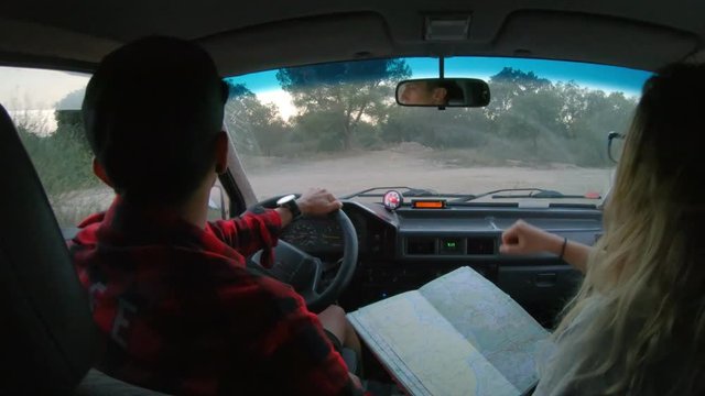 View from backseat on front seat where young hippie or adventure nomad hipster couple drives and navigates camping van with old school paper map, gets lost and finds right route