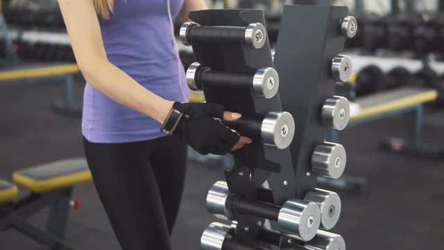 Fit caucasian girl, in purple vest and black leggins, taking small barbells at the gym, slowmotion